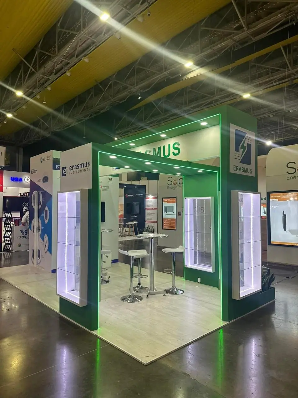 Stand de feria verde con iluminación LED perimetral, vitrinas iluminadas y mesa alta
