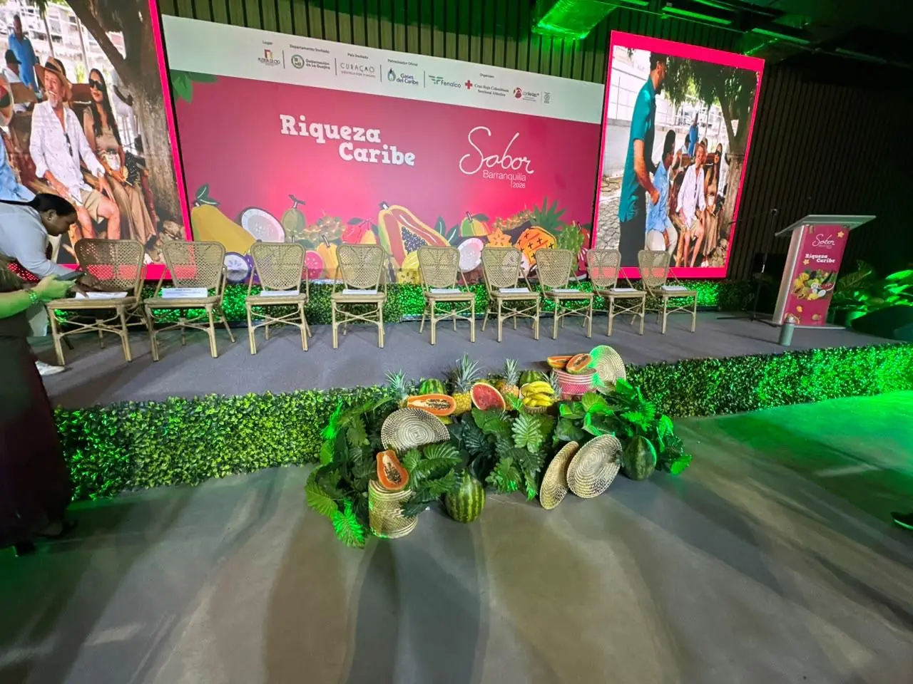 Tarima para evento empresarial con pantalla LED de gran formato, sillas para panelistas, atril y decoración tropical